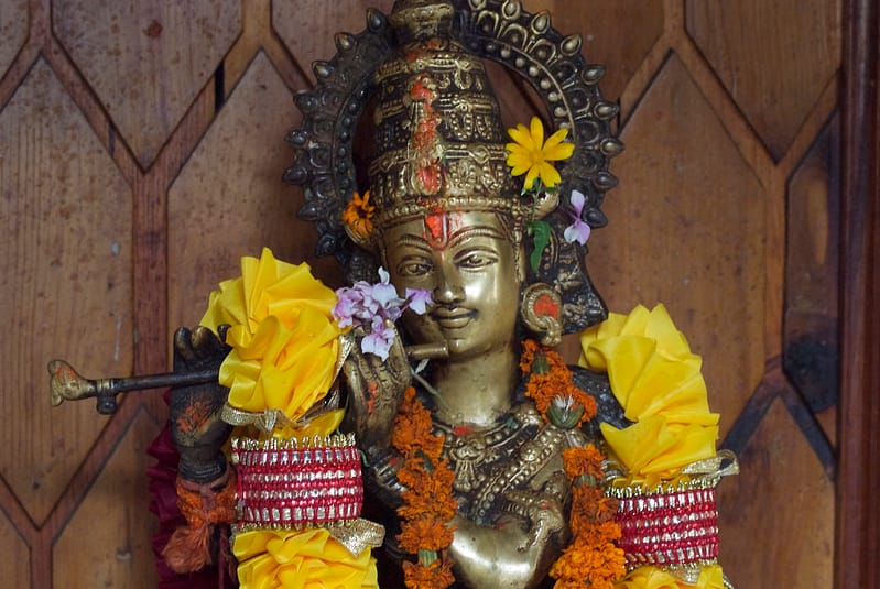 Statue de Krishna jouant de la flûte et décorée de fleurs en Inde