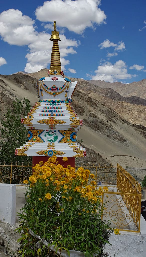 Stupa orné de motifs colorés et de fleurs éclatantes, se dressant avec grâce face aux montagnes minérales et au ciel immense