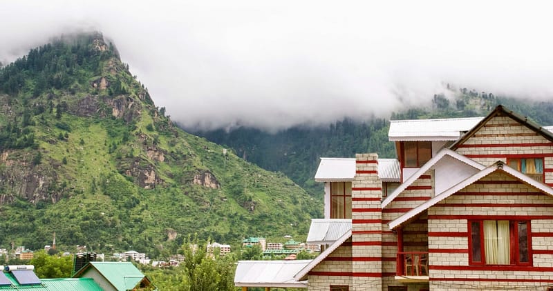 Maisons paisibles nichées au pied des montagnes embrumées, où la nature semble doucement envelopper le quotidien (?)