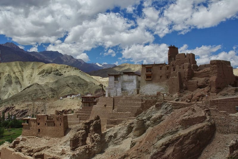 Monastère fortifié en terre et pierre accroché à la montagne, sous un ciel aux nuages sculptés (?)