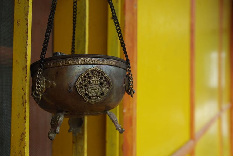 Brûleur d’encens en métal suspendu devant un mur jaune, témoin discret de rituels paisibles (?)