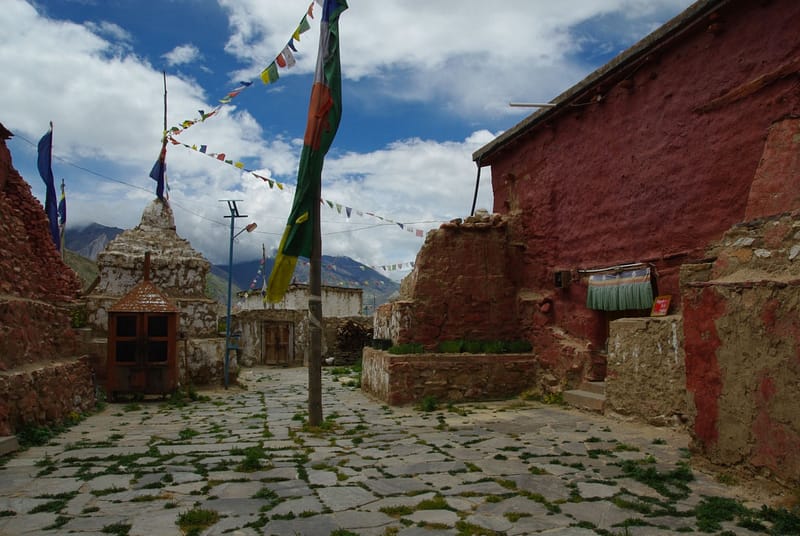 Cour de village de montagne avec stupas, maisons en terre et drapeaux de prière colorés (?)