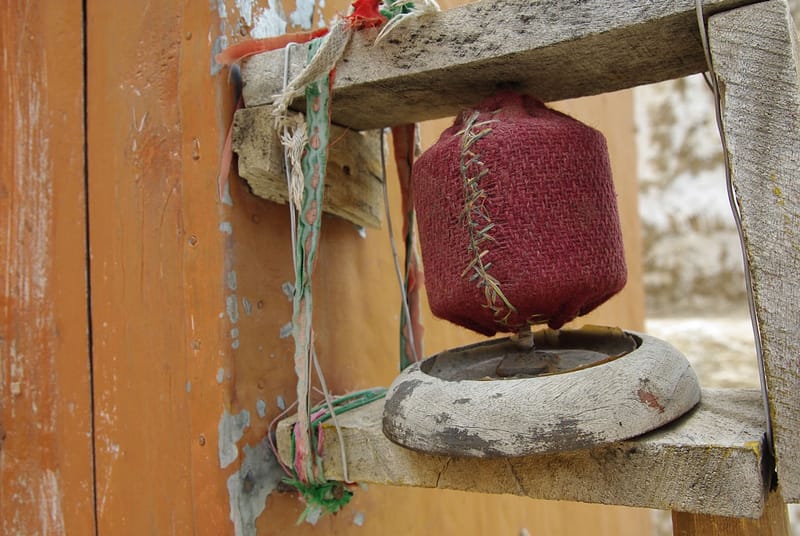 Petit moulin à prière artisanal enveloppé de tissu rouge fixé sur une structure en bois (?)