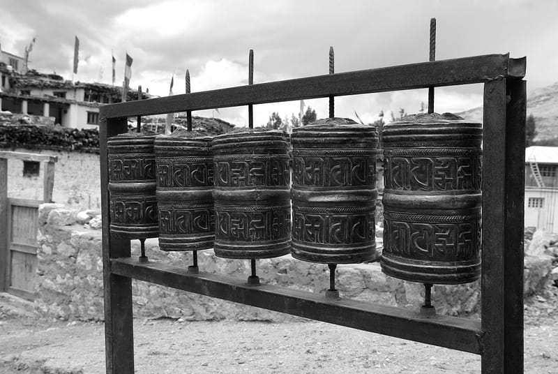 Moulins à prières alignés en métal devant un village de montagne