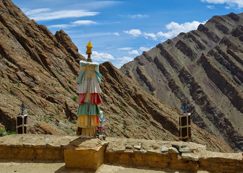 Totems rituels colorés dressés face aux montagnes arides, comme des sentinelles silencieuses entre ciel et pierre (?)